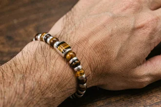 Bracelet homme en oeil du tigre et argent posé sur une surface en bois, détail des pierres et perles métalliques