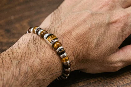 Bracelet homme en oeil du tigre et argent posé sur une surface en bois, détail des pierres et perles métalliques