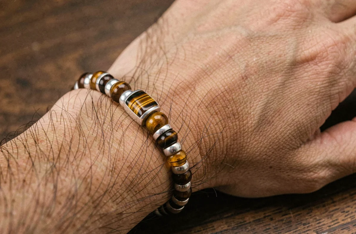 Bracelet homme en oeil du tigre et argent posé sur une surface en bois, détail des pierres et perles métalliques