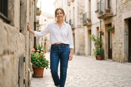 Femme portant un chemisier blanc en coton et un jean brut dans une rue pavée européenne, tenue casual chic décontractée